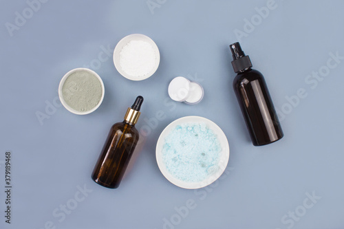 Sea salt, serum in brown dropper glass and spray bottle, clay mask, cream flat lay on blue background top view. Spa products composition. Organic, bio, natural body cosmetic. Beauty, skincare concept.