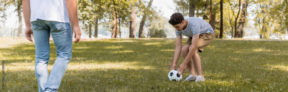 panoramic crop of teenager boy playing football with father