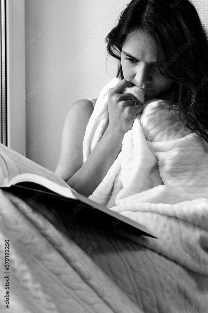 beautiful young woman reads a book on the windowsill and reacts emotionally. black and white image beautiful young woman reads a book on the windowsill and reacts emotionally. black and white image