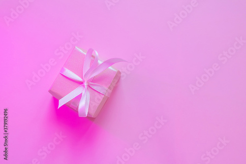 Small square gift in pink wrapping paper with ribbon on pink background, neon lighting. The concept of holiday, presentation, new year, christmas, birthday, celebration. Copspace, flat lay, minimalism © Ольга Холявина