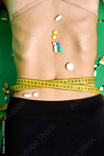 Slim woman's waist wrapped with measure tape. Pills on a female stomach. Concept of weight loss using madicine. photo