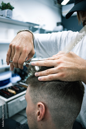 Barber cutting hair of client while working in barbershop 