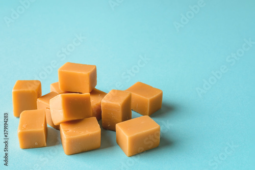 Heap of caramel vanilla fudge on a turquoise background. Fresh tasty candies made of milk and sugar. Square pieces of delicious chewy soft sweets.