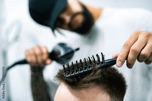 Selective focus of hairstylist using comb while drying hair of man in barbershop 