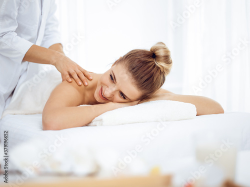 Young and blonde woman enjoying massage of back in spa salon. Beauty concept