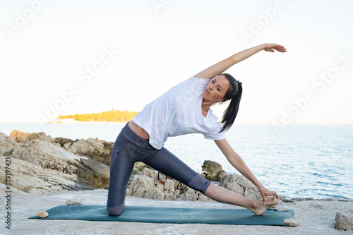 Gorgeous fit brunette woman in yoga pose on the beach during sunrise