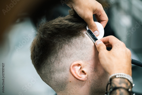 Selective focus of barber trimming young man with sharp folding razor during haircut 