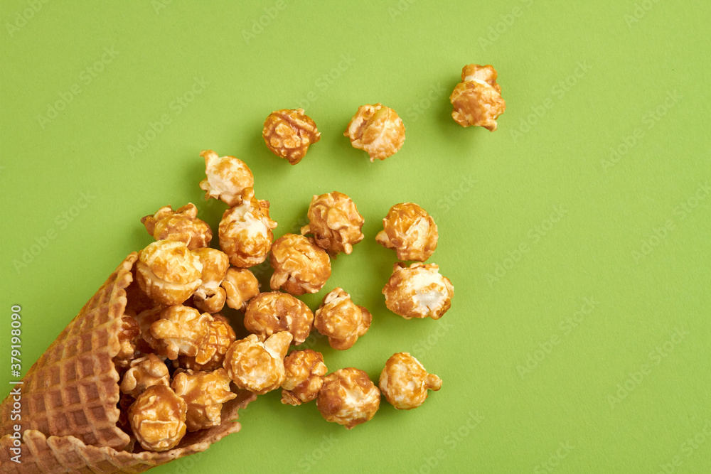 Sweet popcorn in an ice cream wafer. Top view sprinkled corns on green surface. Sweet popcorn in an ice cream wafer. Top view sprinkled corns on green surface.