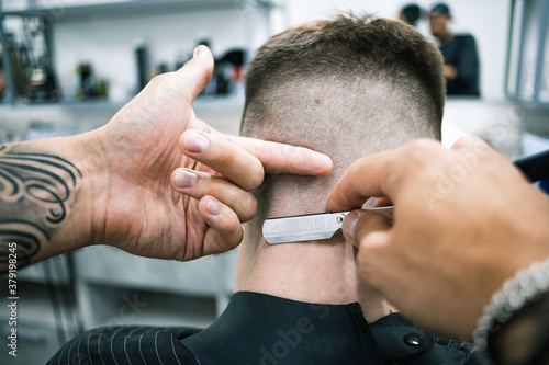 Selective focus of barber using folding shaving razor on neck of client in barbershop 