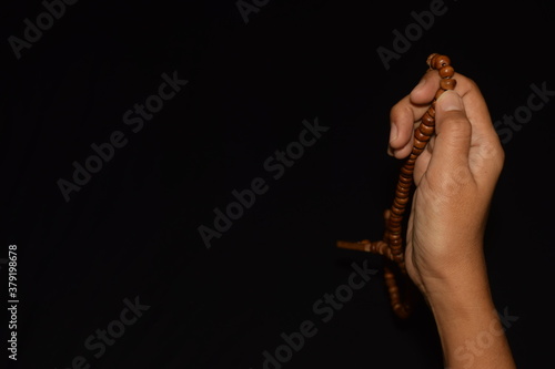 Women's hand holding muslim beads rosery or tasbih over dark background.