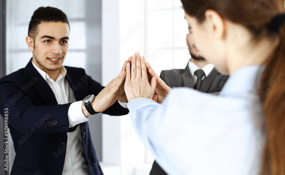 Business people group showing teamwork, joining hands and giving five to each other in modern office. Success concept