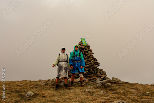 Принти на полотні Tourists in raincoats stand on top of the mountain, Mount Brebeneskul and fog, rain clouds on the Montenegrin ridge, happy tourists