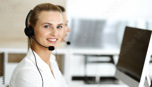 Blond female customer service representative and her colleague are consulting clients online using headset. Call center and business people concept