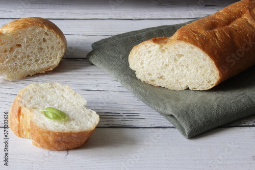 French fresh soft bread baguette on napkin and wooden background. Several cut pieces are lying next to each other. photo