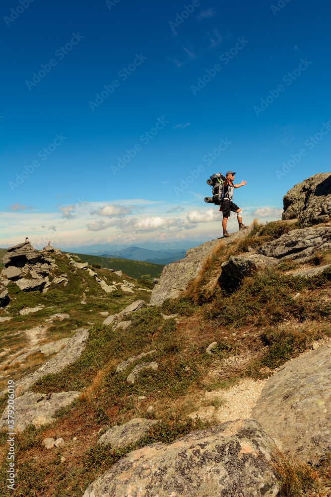 Young man with a backpack standing on top of a mountain and enjoying the view of the valley, the top of the Carpathians Eared stone.