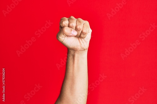 Arm of caucasian white young man over red isolated background doing protest and revolution gesture, fist expressing force and power