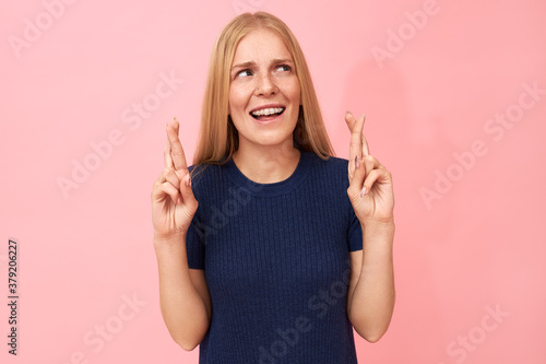 Isolated image of superstitious young woman with teeth braces looking up making hand gesture to protect herself against bad luck or evil, wishing for favor, hoping all her dreams come true
