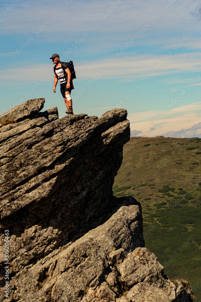 Fototapeta premium traveler, tourist, traveler stands on top of a cliff and enjoys a sunny day and a view of the picturesque Carpathians.