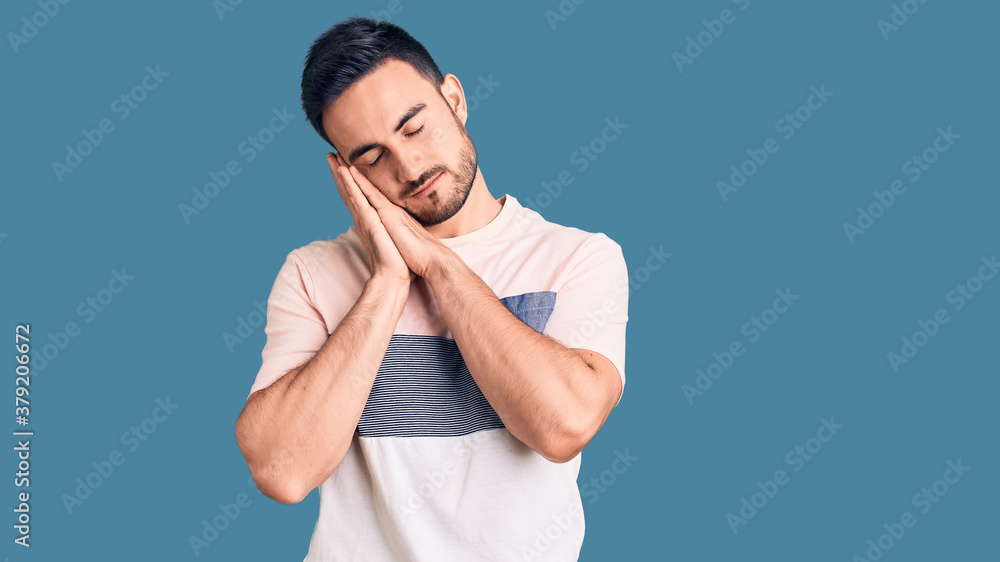 Young handsome man wearing casual clothes sleeping tired dreaming and posing with hands together while smiling with closed eyes. Young handsome man wearing casual clothes sleeping tired dreaming and posing with hands together while smiling with closed eyes.