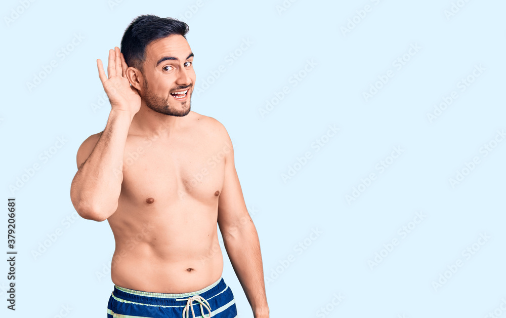 Young handsome man wearing swimwear smiling with hand over ear listening an hearing to rumor or gossip. deafness concept.