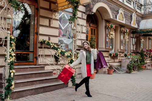 Happy woman is holding gift box in her hands and smiling leaving the store. Beautiful happy girl posing with Christmas presents. New Year preparation © volody10