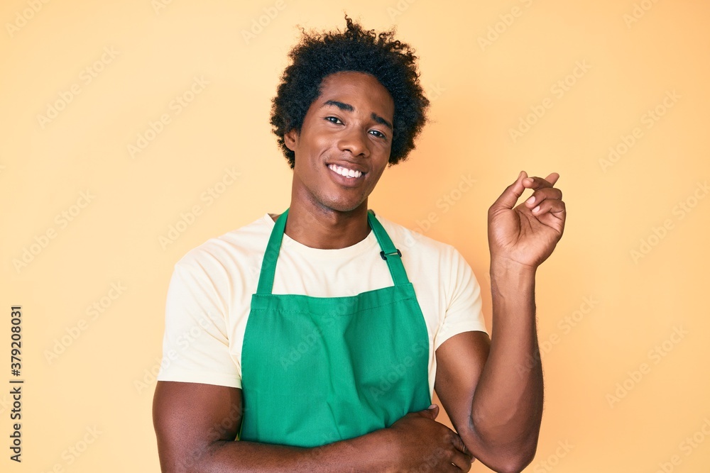 Handsome african american man with afro hair wearing waiter apron smiling happy pointing with hand and finger to the side Handsome african american man with afro hair wearing waiter apron smiling happy pointing with hand and finger to the side