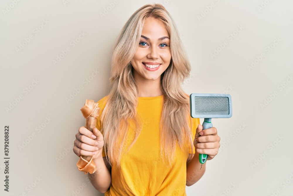 Beautiful caucasian blonde girl holding dog accesories smiling with a happy and cool smile on face. showing teeth. Beautiful caucasian blonde girl holding dog accesories smiling with a happy and cool smile on face. showing teeth.