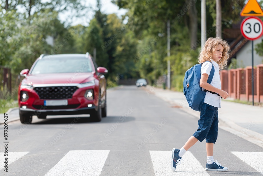 Young boy with a backpack goes through the pedestrian crossing, red cars let him through Young boy with a backpack goes through the pedestrian crossing, red cars let him through