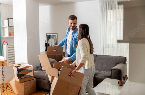 Smiling young couple move into a new home carrying boxes of belongings.