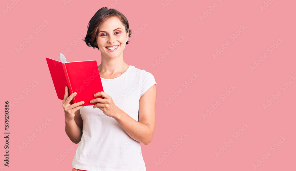 Beautiful young woman with short hair reading a book looking positive and happy standing and smiling with a confident smile showing teeth Beautiful young woman with short hair reading a book looking positive and happy standing and smiling with a confident smile showing teeth