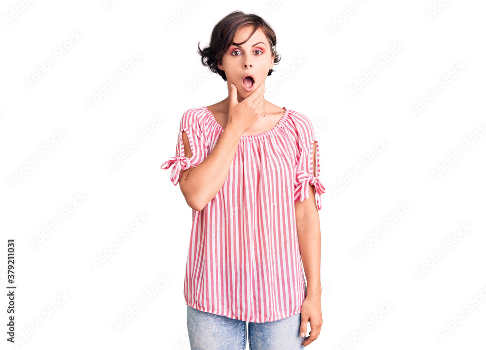 Beautiful young woman with short hair wearing casual summer clothes looking fascinated with disbelief, surprise and amazed expression with hands on chin Beautiful young woman with short hair wearing casual summer clothes looking fascinated with disbelief, surprise and amazed expression with hands on chin