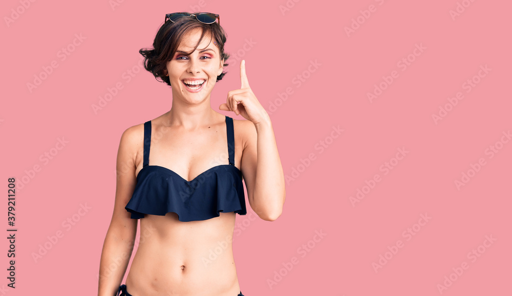 Obraz premium Beautiful young woman with short hair wearing bikini pointing finger up with successful idea. exited and happy. number one.
