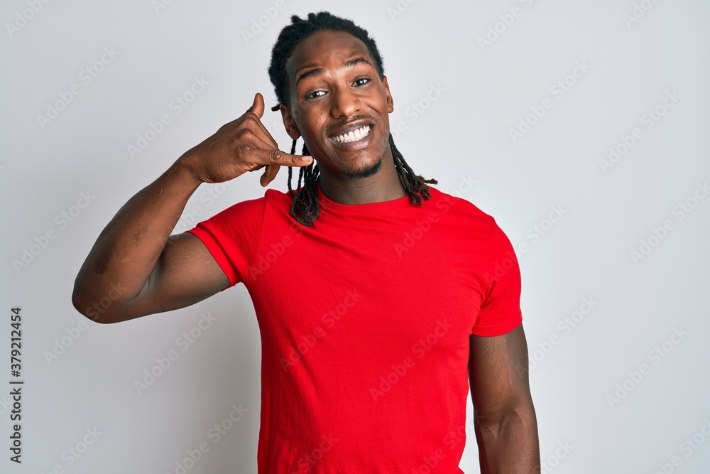 Fototapeta premium African american man with braids wearing casual clothes smiling doing phone gesture with hand and fingers like talking on the telephone. communicating concepts.