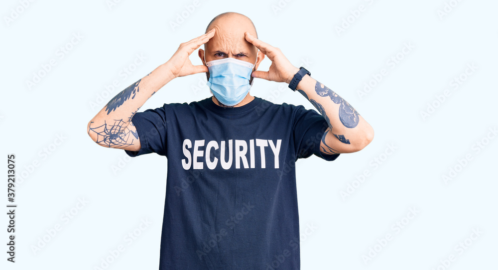 Young handsome man wearing security t shirt and medical mask suffering from headache desperate and stressed because pain and migraine. hands on head.