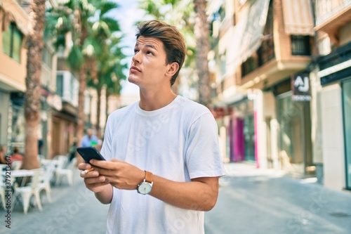 Young caucasian man with serious expression using smartphone and smoking cigarette at the city.