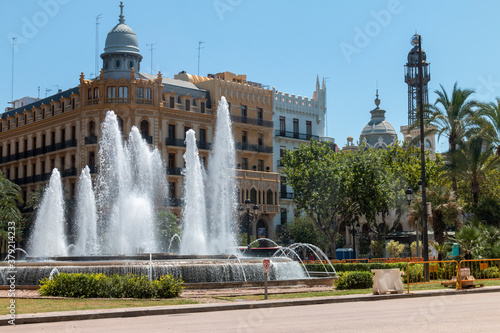 Architecture. Public fountain in a square throwing water in front of beautiful old buildings on a street in Valencia, Spain.
