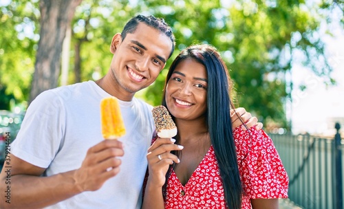 Young latin couple smiling happy eating ice cream at the park.