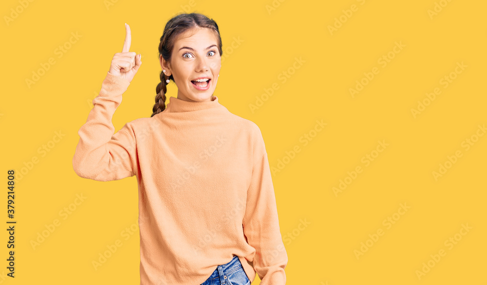 Beautiful caucasian woman with blonde hair wearing casual winter sweater pointing finger up with successful idea. exited and happy. number one. Beautiful caucasian woman with blonde hair wearing casual winter sweater pointing finger up with successful idea. exited and happy. number one.