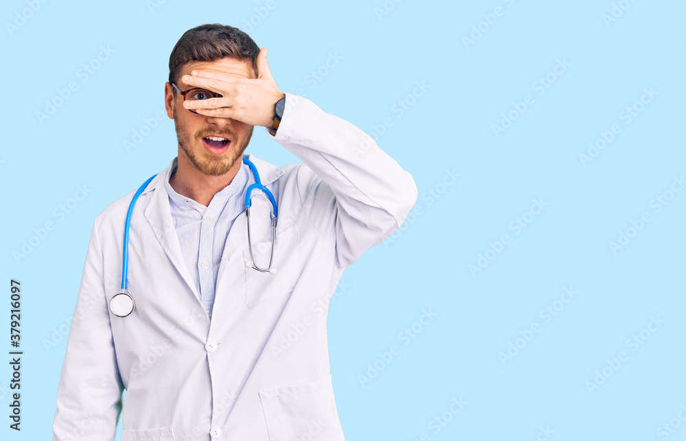 Handsome young man with bear wearing doctor uniform peeking in shock covering face and eyes with hand, looking through fingers with embarrassed expression. Handsome young man with bear wearing doctor uniform peeking in shock covering face and eyes with hand, looking through fingers with embarrassed expression.