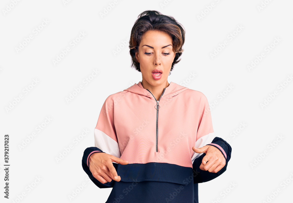 Young beautiful woman wearing sportswear pointing down with fingers showing advertisement, surprised face and open mouth Young beautiful woman wearing sportswear pointing down with fingers showing advertisement, surprised face and open mouth