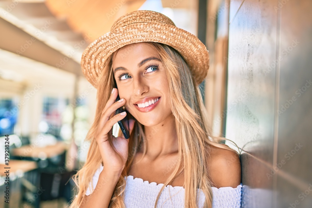 Young blonde tourist girl smiling happy talking on the smartphone leaning on the wall.
