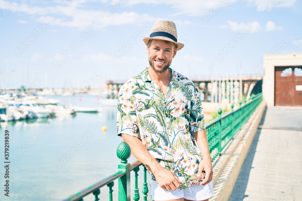 Handsome caucasian man wearing summer hat and flowers shirt smiling happy outdoors