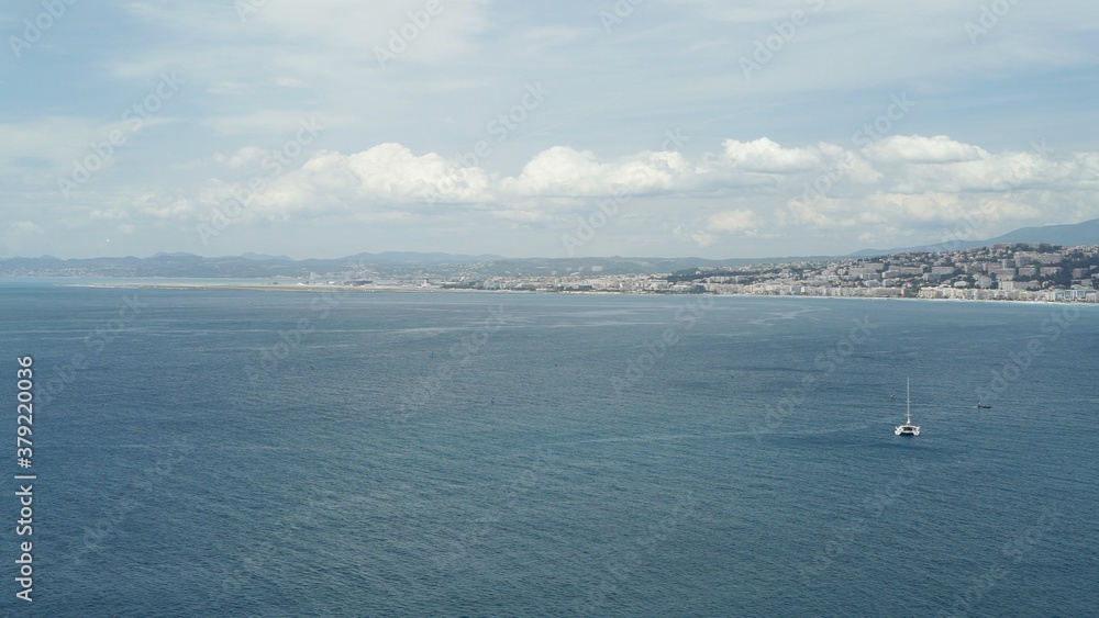 Mediterranean sea in Nice, on background, drone shot of wide blue ocean under cloudy sky. Panoramic view of a city on background with big deep water on foreground