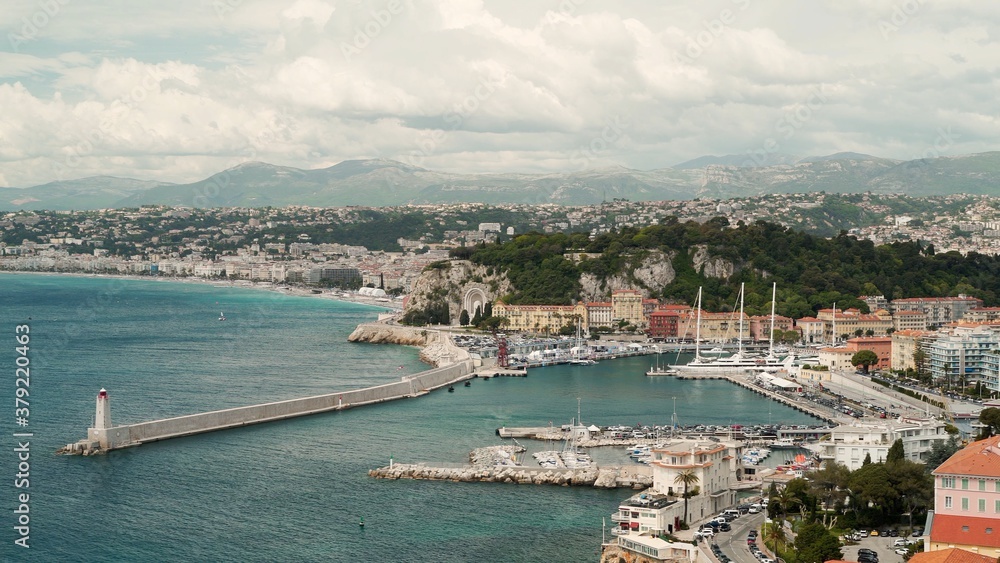 South city of French, Nice with a coastline, houses and lighthouse on a big ocean. Cloudy day, shot from above, a long extended shoreline, cloudy windy day and mountains on background
