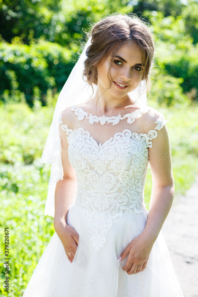 Happy bride in a long white wedding dress and veil in a green park on nature. Wedding image of a young girl, women's makeup and hairstyle. Marriage concept Happy bride in a long white wedding dress and veil in a green park on nature. Wedding image of a young girl, women's makeup and hairstyle. Marriage concept