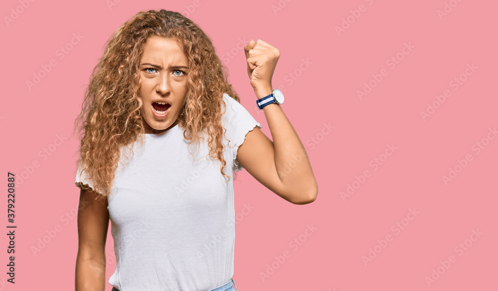 Beautiful caucasian teenager girl wearing casual white tshirt angry and mad raising fist frustrated and furious while shouting with anger. rage and aggressive concept. Beautiful caucasian teenager girl wearing casual white tshirt angry and mad raising fist frustrated and furious while shouting with anger. rage and aggressive concept.