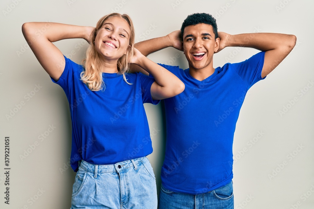 Young interracial couple wearing casual clothes relaxing and stretching, arms and hands behind head and neck smiling happy Young interracial couple wearing casual clothes relaxing and stretching, arms and hands behind head and neck smiling happy