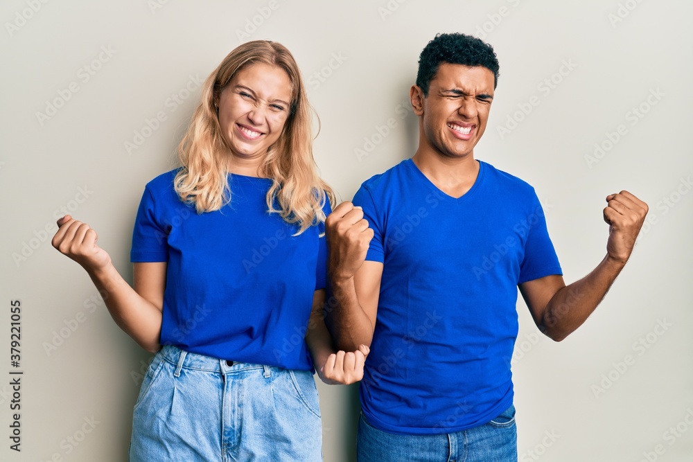 Young interracial couple wearing casual clothes very happy and excited doing winner gesture with arms raised, smiling and screaming for success. celebration concept. Young interracial couple wearing casual clothes very happy and excited doing winner gesture with arms raised, smiling and screaming for success. celebration concept.