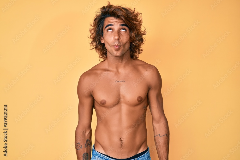 Young hispanic man standing shirtless making fish face with lips, crazy and comical gesture. funny expression.