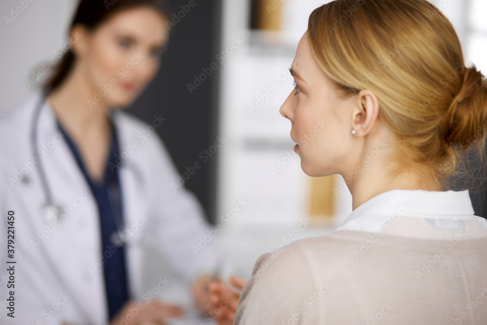 Friendly smiling female doctor and patient woman discussing current health examination while sitting in clinic. Medicine and healthcare concept Friendly smiling female doctor and patient woman discussing current health examination while sitting in clinic. Medicine and healthcare concept